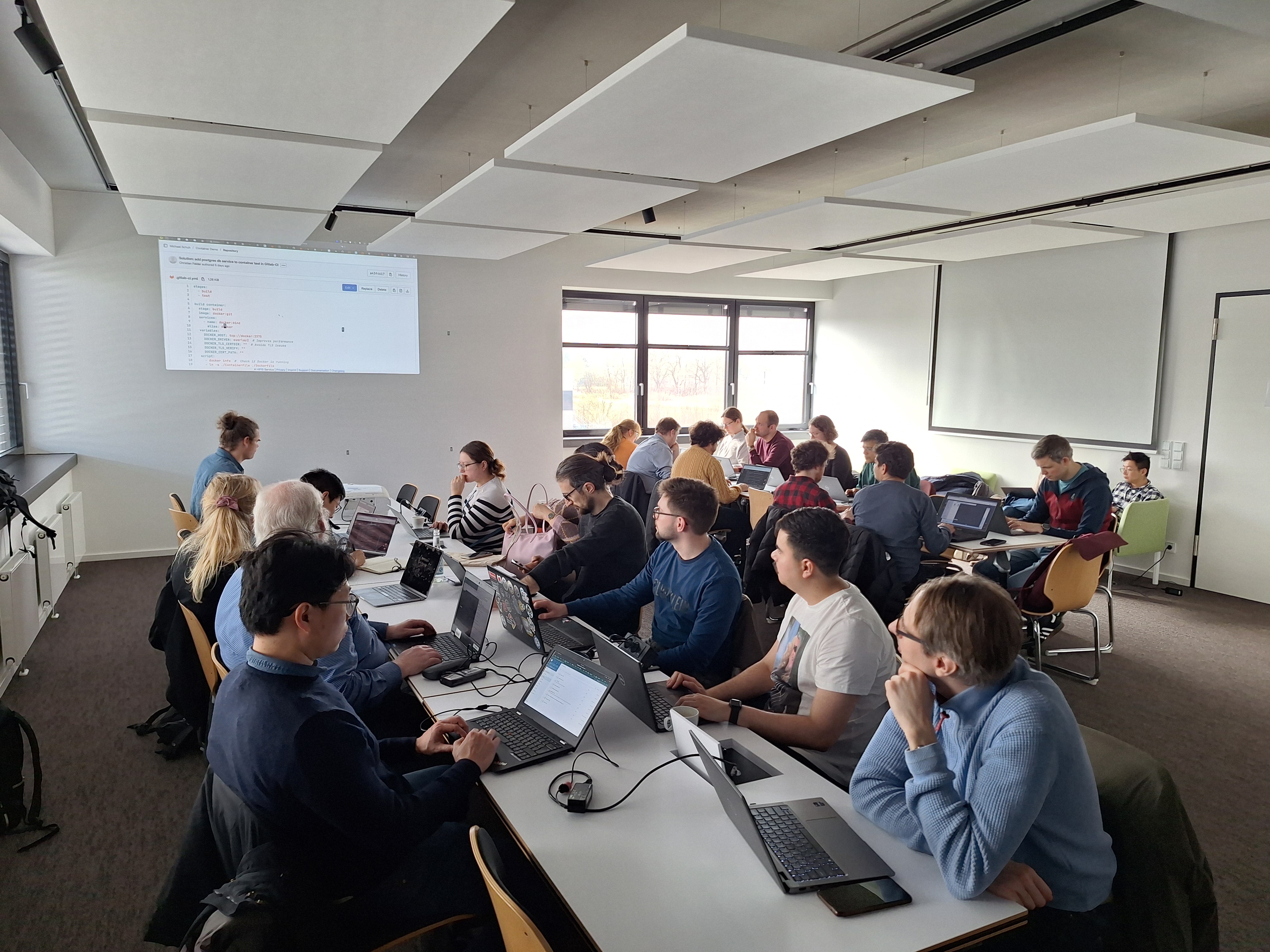 Personen in einem Besprechungsraum mit Laptops und Projektion an der Wand.